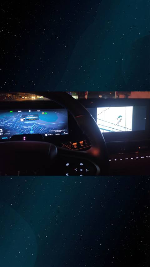 Bir aracın multimedya ekranında navigasyon haritası ve diğer ekranda video oynatılırken direksiyon önünden çekilmiş gece görüntüsü.