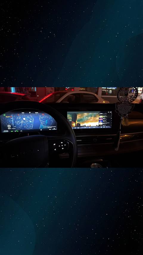 Bir arac icerisinde direksiyon, dijital gosterge paneli ve multimedya ekraninda harita navigasyonu ve gorsel yayin goruntulenirken cam disinda gece trafik gorunumu yer aliyor.