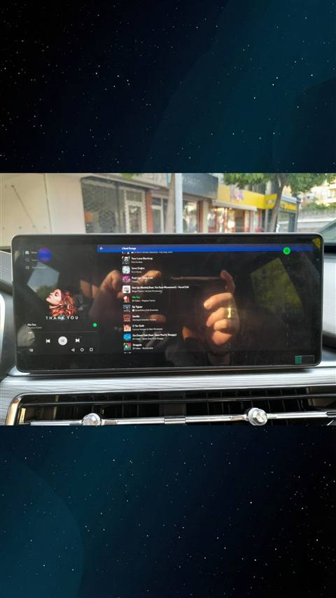 Arac multimedya ekraninda Spotify muzik uygulamasinin acik oldugu, kadi el ile ekrana dogru telefonla fotograf cekildigi bir goruntu.