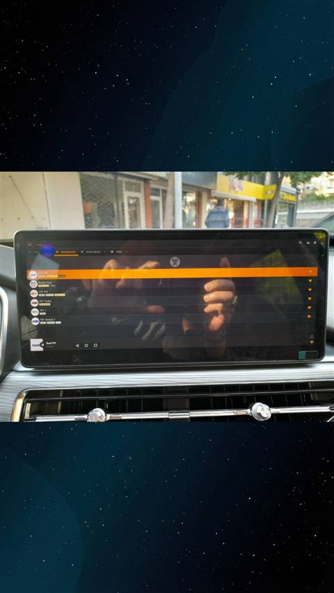 Bir araç multimedya ekranında radyo favorileri listesi (Best FM, Radyo Ego, TRT FM vb.) görüntüleniyor ve ekrana bir el uzanmış durumda.