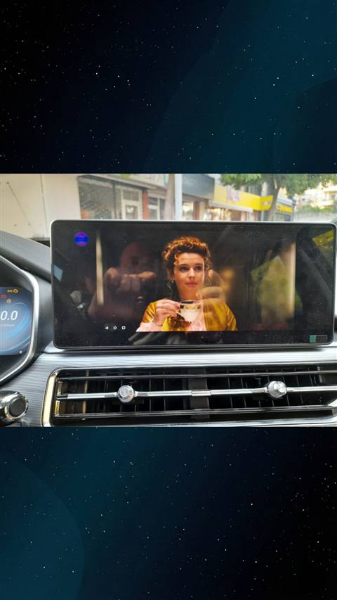 Araç multimedya ekranında bir film/dizi sahnesi izlenirken gösterge paneli ve klima kumandaları görünüyor.