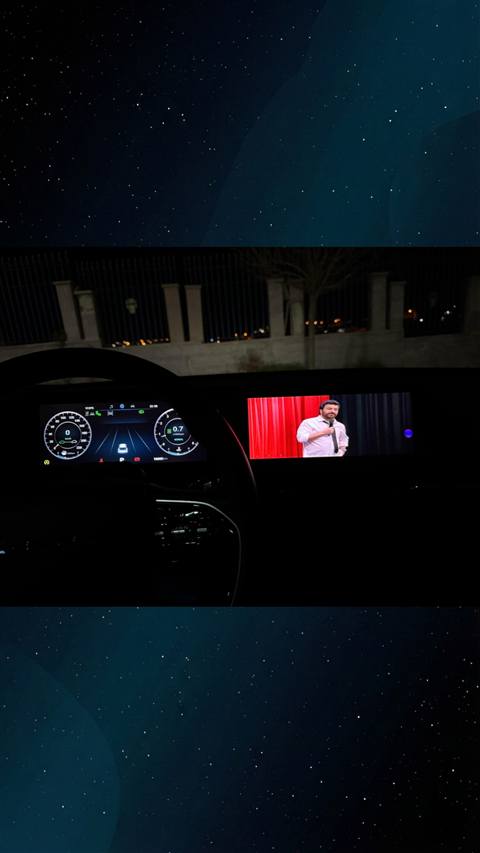 Gece vaktinde araç içinden dijital gösterge paneli ve multimedya ekranında bir stand-up gösterisi izlenirken çekilmiş bir görüntü.